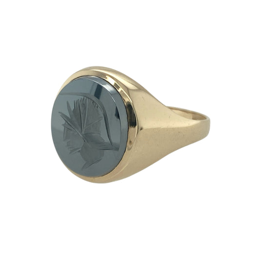 Bring bold character and classic elegance to your collection with this pre-owned 9ct yellow gold and hematite Centurion set oval signet ring, offering a striking blend of strong design and timeless detail—perfect for making a distinguished statement.

Design: The ring features an impressive 13mm by 11mm oval hematite stone engraved with a Centurion motif, creating a bold and eye-catching focal point that exudes strength and heritage.

