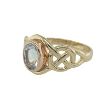 Load image into Gallery viewer, Celebrate heritage and colour with this pre-owned 9ct yellow and rose gold Clogau ring, featuring a vibrant blue topaz and elegant Celtic detailing.

Design: A 7mm by 5mm oval-cut blue topaz sits at the centre of an intricately shaped Celtic design, blending symbolic curves with vivid sparkle.
Material: Made from 9-carat yellow gold with rose gold accents, the ring carries the distinctive Clogau Welsh gold touch, known for its warmth and rarity.

