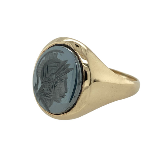 Striking and full of character, this pre-owned 9ct yellow gold hematite centurion signet ring blends bold design with a touch of classical heritage—perfect for those who appreciate statement jewellery with historical flair.

Design: The ring features a 14mm by 12mm oval hematite stone carved with a centurion profile, adding depth, texture, and a distinctive focal point.
Material: Made from 9-carat yellow gold, the polished finish offers a warm contrast to the metallic sheen of the hematite.
