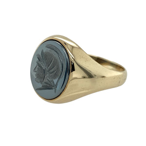Bold and steeped in character, this pre-owned 9ct yellow gold hematite centurion signet ring combines classic craftsmanship with historical style—perfect for those who appreciate timeless strength and detail.

Design: The ring features a 13mm by 11mm oval hematite stone engraved with a detailed centurion profile, offering a striking focal point with vintage appeal.
Material: Made from 9-carat yellow gold, the polished finish contrasts beautifully with the dark metallic sheen of the hematite.
