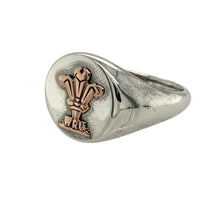 Load image into Gallery viewer, Bring national pride and bold heritage style to your jewellery collection with this pre-owned 925 silver Clogau WRU signet ring, featuring the iconic Three Feathers in 9ct rose gold—perfect for celebrating Welsh identity with timeless presence.

Design: The ring features an oval-shaped front measuring 13mm high, engraved with the official WRU Three Feathers emblem in polished 9ct rose gold for a striking and recognisable finish.

