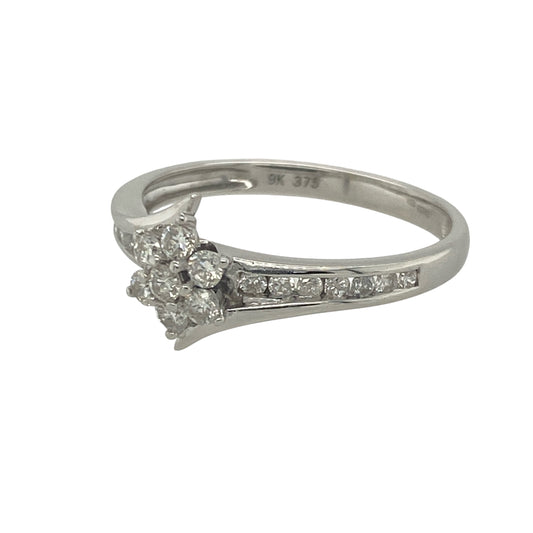 Bring sparkling elegance and timeless charm to your collection with this pre-owned 9ct white gold diamond flower cluster twist ring—a graceful design with refined brilliance.

Design: The ring features a 9mm high floral cluster of diamonds at the centre, complemented by diamond-set shoulders and a subtle twist design for added detail.
Material: Made from 9-carat white gold, the polished finish enhances the brilliance of the diamonds and adds modern appeal.
