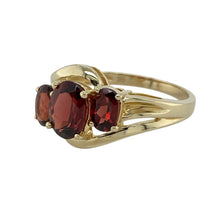 Load image into Gallery viewer, Bring deep colour and elegant style to your collection with this pre-owned 9ct yellow gold garnet trilogy twist ring, combining rich tones with a graceful design—perfect for both everyday wear and special occasions.

Design: The ring features an 8mm by 6mm oval garnet at the centre, accented by two smaller garnets in a classic trilogy layout with a flowing twist detail along the shoulders.

