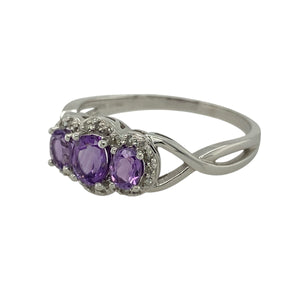 Bring vibrant colour and sparkling detail to your collection with this pre-owned 9ct white gold amethyst and diamond trilogy halo ring, offering timeless elegance with a touch of modern brilliance—perfect for special occasions or refined everyday wear.

Design: The ring features a 5mm by 4mm oval amethyst at the centre, framed by a halo of diamonds and flanked by two smaller amethysts for a balanced trilogy design.
