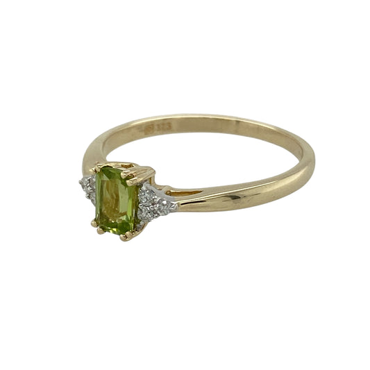 Bring fresh colour and refined sparkle to your collection with this pre-owned 9ct yellow gold peridot and diamond ring—a timeless design combining vibrant gemstones with elegant detail.

Design: The ring features a 6mm by 4mm rectangular peridot at the centre, flanked on each side by three small diamonds for added brilliance and balance.
Material: Made from 9-carat yellow gold, the polished finish complements the vivid green of the peridot and enhances the sparkle of the diamonds.