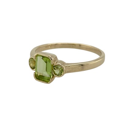 Bring fresh colour and elegant balance to your collection with this pre-owned 9ct yellow gold peridot trilogy ring—a timeless design symbolising past, present, and future.

Design: The ring features a 7mm by 5mm rectangular peridot at the centre, flanked by two 3mm round peridots on either side, creating a harmonious and eye-catching trilogy style.
Material: Made from 9-carat yellow gold, the polished finish enhances the vibrant green of the peridots and adds a warm golden glow.