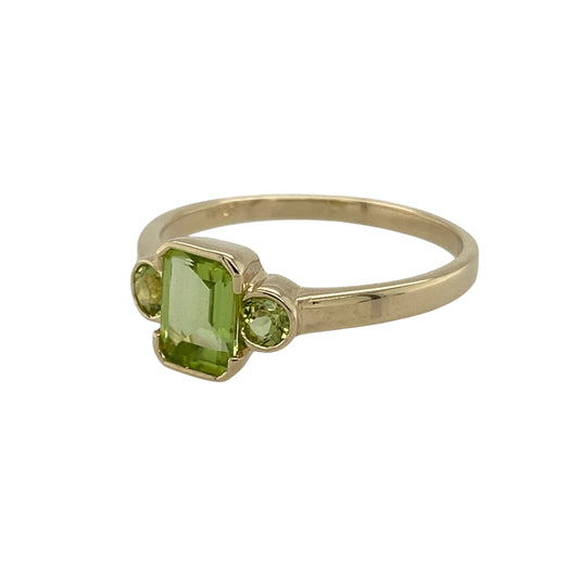 Bring fresh colour and elegant balance to your collection with this pre-owned 9ct yellow gold peridot trilogy ring—a timeless design symbolising past, present, and future.

Design: The ring features a 7mm by 5mm rectangular peridot at the centre, flanked by two 3mm round peridots on either side, creating a harmonious and eye-catching trilogy style.
Material: Made from 9-carat yellow gold, the polished finish enhances the vibrant green of the peridots and adds a warm golden glow.