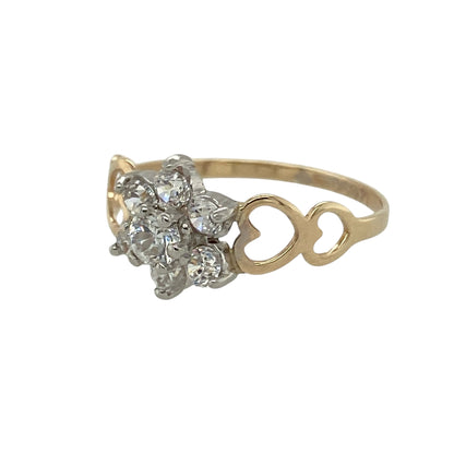 Bring sparkling charm and romantic detail to your collection with this pre-owned 9ct yellow gold cubic zirconia flower cluster ring—a classic design with a delicate, feminine touch.

Design: The ring features a 9mm high flower cluster of cubic zirconia stones, with cut-out heart shapes on the shoulders adding extra character and charm.
Material: Made from 9-carat yellow gold with cubic zirconia, the polished finish enhances the brilliance of the stones and the warmth of the gold.