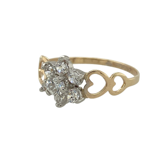 Bring sparkling charm and romantic detail to your collection with this pre-owned 9ct yellow gold cubic zirconia flower cluster ring—a classic design with a delicate, feminine touch.

Design: The ring features a 9mm high flower cluster of cubic zirconia stones, with cut-out heart shapes on the shoulders adding extra character and charm.
Material: Made from 9-carat yellow gold with cubic zirconia, the polished finish enhances the brilliance of the stones and the warmth of the gold.