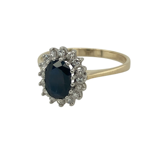 Bring timeless elegance and vibrant colour to your collection with this pre-owned 9ct yellow gold diamond and sapphire cluster ring—an eye-catching piece that combines deep blue tones with sparkling brilliance.

Design: The ring features a 7mm by 5mm oval-cut sapphire at the centre, surrounded by a cluster of round brilliant-cut diamonds for a radiant and classic finish.
Material: Made from 9-carat yellow gold, the polished band enhances the rich blue sapphire and the sparkle of the diamonds.