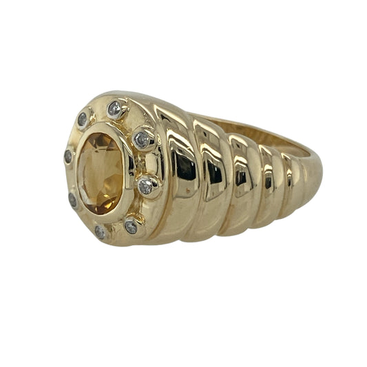 Bring warm colour and bold sophistication to your collection with this pre-owned 9ct yellow gold diamond and citrine signet ring, combining a striking gemstone with refined detailing.

Design: The ring showcases an 8mm by 6mm oval-cut citrine at the centre, framed by a halo of sparkling diamonds and enhanced by ribbed texture shoulders for added character.