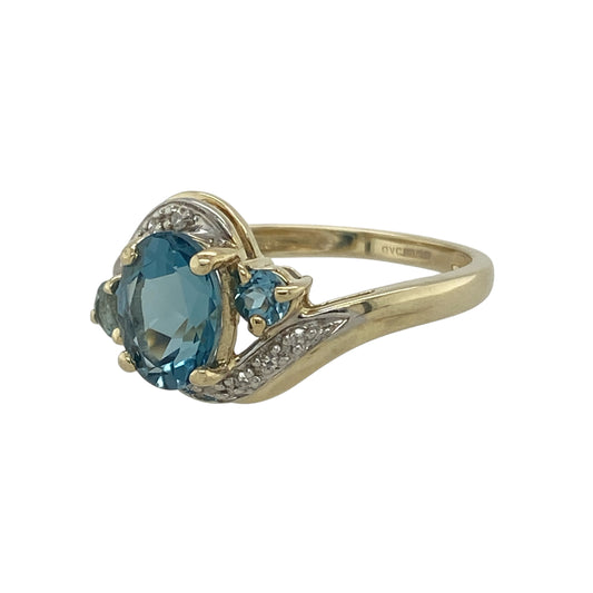 Bring radiant colour and graceful style to your collection with this pre-owned 9ct yellow gold diamond and blue topaz twist ring, blending elegance with a touch of sparkle.

Design: The ring showcases an 8mm by 6mm oval-cut blue topaz at the centre, flanked by two smaller round topaz stones and accented with diamonds along the twist design for added brilliance.
Material: Made from 9-carat yellow gold, the polished finish enhances the cool blue tones of the topaz and the sparkle of the diamonds.
