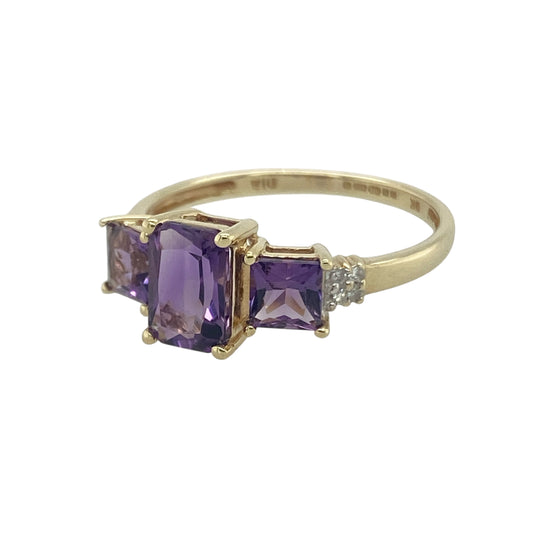 Bring vibrant colour and refined sparkle to your collection with this pre-owned 9ct yellow gold diamond and amethyst trilogy ring, a timeless design with elegant detail.

Design: The ring features a 7mm by 5mm rectangular amethyst at the centre, flanked by two square-cut amethysts on either side, with sparkling diamonds set into the shoulders for added brilliance.
Material: Made from 9-carat yellow gold, the polished finish enhances the rich purple tones of the amethysts and the sparkle of the diamonds.