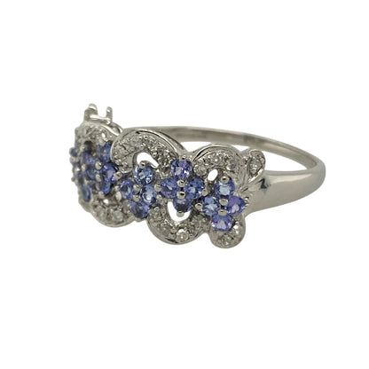 Bring colour, sparkle, and graceful design to your collection with this pre-owned 9ct white gold diamond and tanzanite flower cluster swirl ring—a striking piece that captures elegance with a modern twist.

Design: The ring features a flower-shaped cluster of violet-blue tanzanite stones surrounded by sparkling diamonds, all arranged in a flowing swirl pattern that enhances the ring’s movement and brilliance. The combination of soft colour and sparkle creates a refined, feminine look.