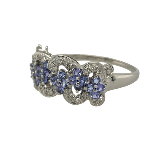 Bring colour, sparkle, and graceful design to your collection with this pre-owned 9ct white gold diamond and tanzanite flower cluster swirl ring—a striking piece that captures elegance with a modern twist.

Design: The ring features a flower-shaped cluster of violet-blue tanzanite stones surrounded by sparkling diamonds, all arranged in a flowing swirl pattern that enhances the ring’s movement and brilliance. The combination of soft colour and sparkle creates a refined, feminine look.