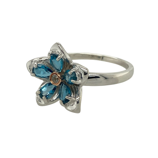 Celebrate nature-inspired beauty and delicate sparkle with this pre-owned 925 silver and 9ct rose gold Clogau flower ring, blending graceful design with vibrant gemstones—perfect for adding a touch of elegance to any look.

Design: The ring showcases a charming floral motif measuring 15mm high, featuring vivid blue topaz stones as the petals and a brilliant white topaz at the centre, creating a radiant and feminine composition.