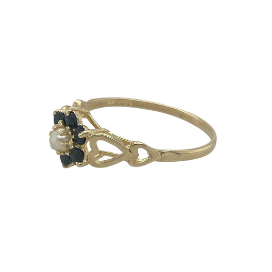 Add vintage-inspired charm and delicate beauty to your collection with this pre-owned 9ct yellow gold sapphire and pearl flower cluster ring, combining timeless elegance with soft, graceful detail—perfect for special occasions or refined everyday wear.

Design: The ring features a central 3mm sapphire surrounded by dainty seed pearls arranged in a floral cluster, creating a classic and feminine look.
