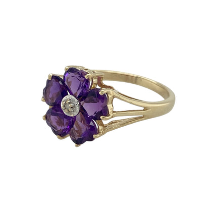 Bring feminine charm and vibrant colour to your collection with this pre-owned 9ct gold diamond and amethyst flower ring—an enchanting piece offering delicate sparkle, floral elegance, and timeless appeal.

Design: This size O ring features a 12mm high floral arrangement formed from heart-shaped amethyst stones that create the petals, with a small diamond set at the centre for a subtle, sparkling finish.