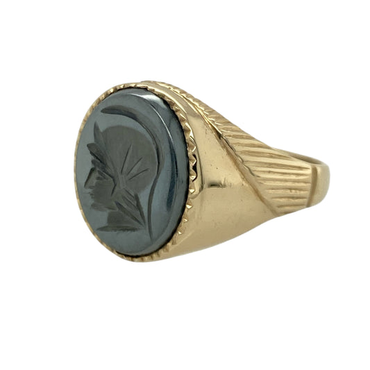 Bring bold character and striking contrast to your collection with this pre-owned 9ct yellow gold hematite centurion signet ring—an impressive piece offering strong presence and timeless appeal.

Design: This size W signet ring features a 14mm by 11mm oval hematite stone engraved with a classic centurion motif, creating a distinctive, detailed focal point with a deep metallic sheen.