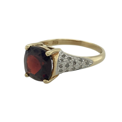 Bring rich colour and elegant sparkle to your collection with this pre-owned 9ct yellow and white gold garnet and diamond ring—an attractive piece offering timeless beauty and refined contrast.

Design: This size L ring features an 8mm by 8mm cushion-cut garnet at the centre, showcasing its deep red hue, enhanced by diamond accents that add bright, balanced sparkle.