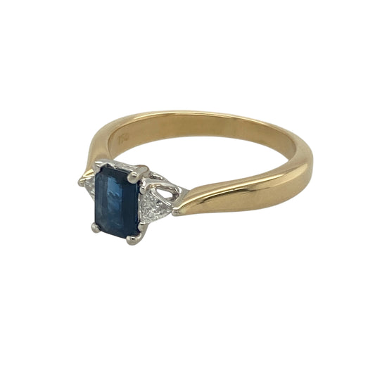 Bring refined colour and elegant sparkle to your collection with this pre-owned 18ct yellow gold sapphire and diamond trilogy ring—an exquisite piece offering timeless beauty and sophisticated detail.

Design: This size M–N ring features a 6mm by 4mm emerald-cut sapphire at the centre, framed by a trillion-cut diamond on either side to create a striking and beautifully balanced trilogy arrangement.
