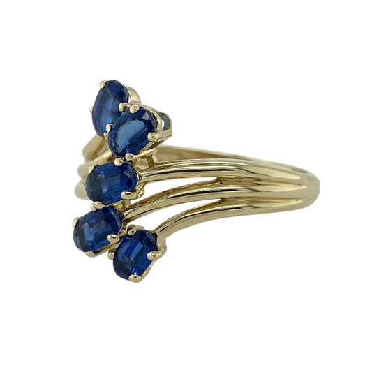 Bring rich colour and elegant styling to your collection with this pre-owned 9ct yellow gold sapphire split band ring—an eye-catching piece with timeless gemstone appeal.

Design: The front of the ring stands 17mm high and features five 5mm by 3mm oval sapphire stones arranged along a graceful split band. The flowing design enhances the deep blue colour of the sapphires, creating a striking and balanced look on the finger.