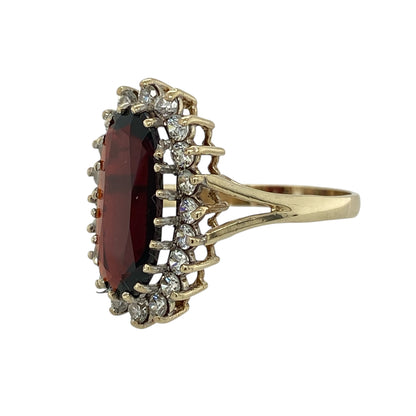 Bring rich colour and eye-catching sparkle to your jewellery collection with this pre-owned 9ct yellow gold garnet and cubic zirconia set cluster ring, a bold design with elegant presence and classic appeal.

Design: The ring features a large oval garnet-coloured centre stone measuring approximately 15mm by 7mm, surrounded by clear cubic zirconia accents that enhance its deep red tone and create a striking cluster effect.