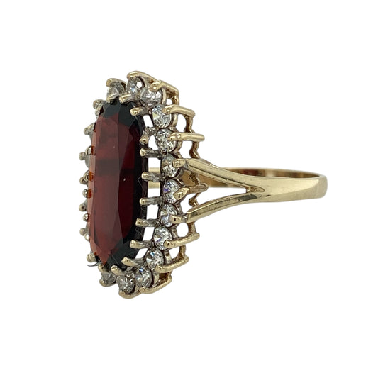 Bring rich colour and eye-catching sparkle to your jewellery collection with this pre-owned 9ct yellow gold garnet and cubic zirconia set cluster ring, a bold design with elegant presence and classic appeal.

Design: The ring features a large oval garnet-coloured centre stone measuring approximately 15mm by 7mm, surrounded by clear cubic zirconia accents that enhance its deep red tone and create a striking cluster effect.