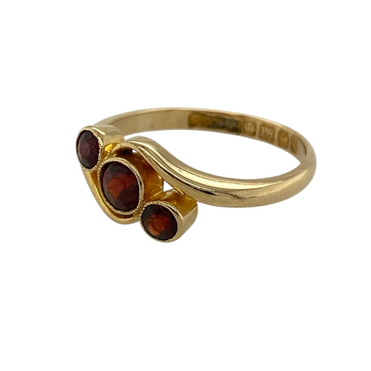 Bring rich colour and elegant movement to your jewellery collection with this pre-owned 18ct yellow gold garnet set trilogy twist ring, a graceful design that blends classic symbolism with a flowing silhouette.

Design: The ring features a trilogy arrangement of garnet stones, with a 4mm centre stone flanked by two 3mm garnets, set within a gently twisting band that adds softness and visual interest.