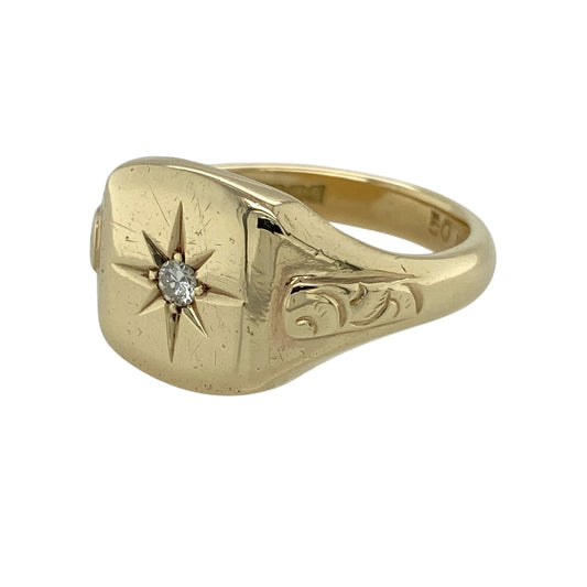 Bring bold character and refined sparkle to your jewellery collection with this pre-owned 9ct yellow gold diamond starburst signet ring, a striking design that blends traditional form with decorative detail.

Design: The ring features a classic signet-style face with a starburst motif, centred with a diamond of approximately 0.11ct. The front measures 13mm high, giving the ring a strong and confident presence, while the shoulders are finished with an attractive patterned design.
