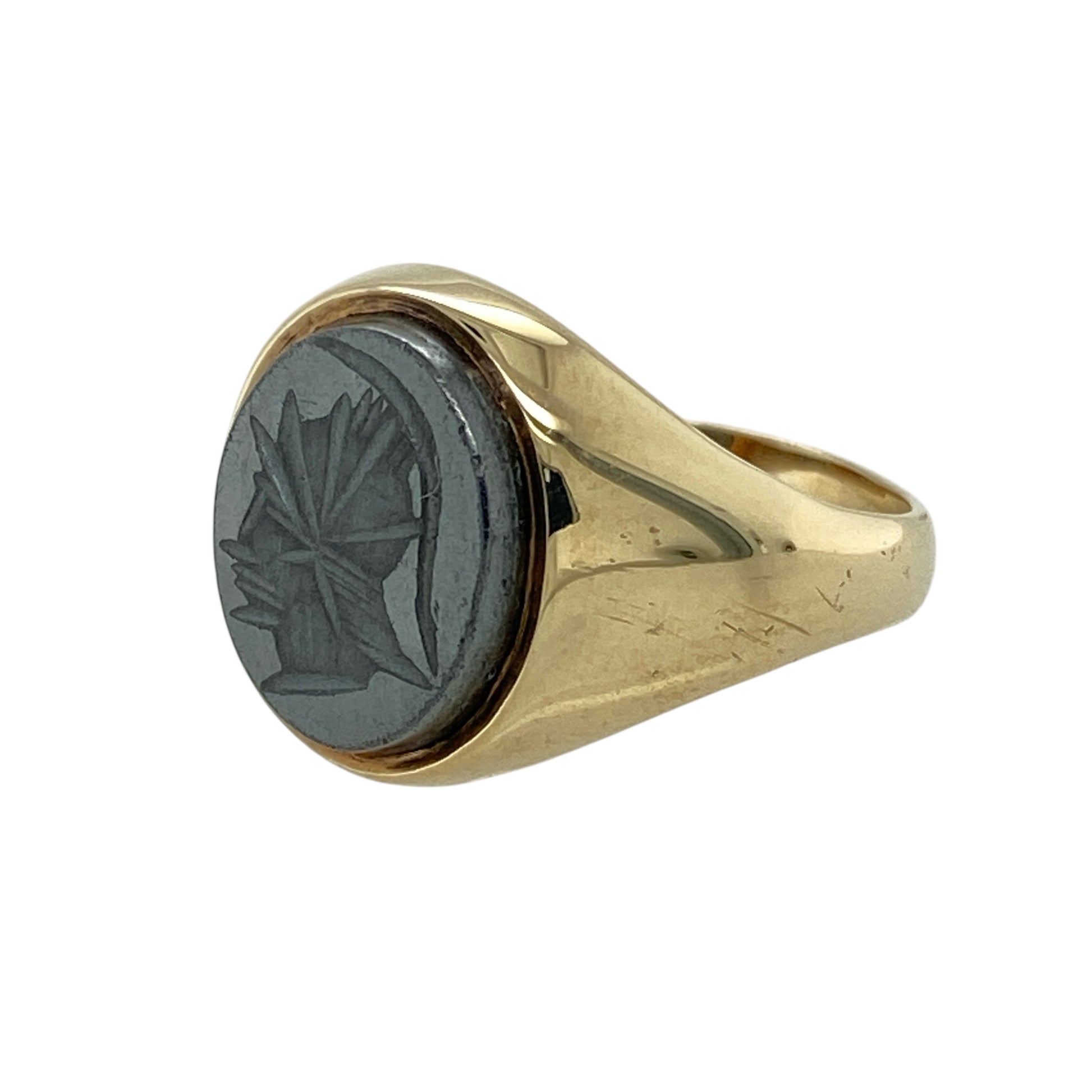 Bring bold character and classical inspiration to your jewellery collection with this pre-owned 9ct yellow gold hematite centurion set oval signet ring, a striking design with strong presence.

Design: The ring features an oval hematite stone measuring 11mm by 9mm, engraved with a centurion motif that creates a powerful and distinctive focal point.
Material: Made from polished 9-carat yellow gold, the warm tone provides a rich contrast to the dark, reflective surface of the hematite.