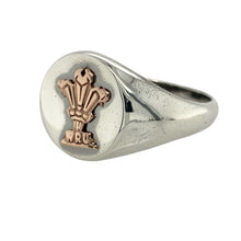 Load image into Gallery viewer, Bring national pride and bold heritage style to your jewellery collection with this pre-owned 925 silver Clogau WRU signet ring, featuring the iconic Three Feathers in 9ct rose gold—perfect for celebrating Welsh identity with timeless presence.

Design: The ring features an oval-shaped front measuring 13mm high, engraved with the official WRU Three Feathers emblem in polished 9ct rose gold for a striking and recognisable finish.

