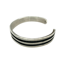 Load image into Gallery viewer, Bring bold contrast and modern edge to your collection with this pre-owned 925 silver black line detail cuff bangle, offering a sleek and structured design—perfect for everyday sophistication or statement styling.

Design: The bangle features a wide cuff profile with recessed black line detailing, adding depth and a contemporary finish to its clean, minimal silhouette.
Material: Made from 925 sterling silver, the polished surface contrasts beautifully
