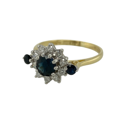 Bring classic colour and refined sparkle to your jewellery collection with this pre-owned 18ct yellow gold diamond and sapphire set cluster ring, offering a timeless design with elegant gemstone detailing—perfect for everyday wear or special occasions.

Design: The ring features a round sapphire at the centre measuring approximately 5mm in diameter, surrounded by diamonds totalling around 0.20ct. A sapphire accent on each shoulder adds balance and extra colour to the design.
