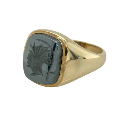 Make a commanding statement with this pre-owned 9ct yellow gold and hematite Centurion signet ring, a bold and characterful piece ideal for those who appreciate distinctive and traditional gold jewellery.

Design: The ring features a striking rectangular hematite stone measuring approximately 14mm by 12mm, engraved with a detailed Centurion motif. The dark metallic sheen of the hematite creates dramatic contrast against the warm yellow gold, giving the ring strong presence on the finger.