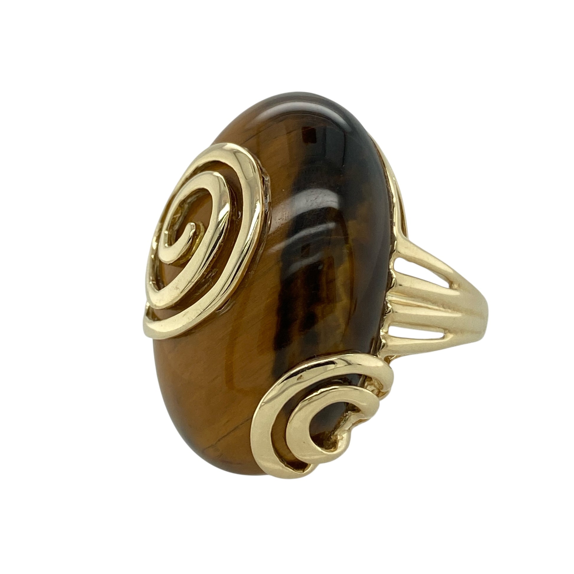 Make a bold and distinctive statement with this pre-owned 9ct yellow gold and Tiger’s Eye set swirl ring—an impressive piece designed to stand out.

Design: The ring features a striking oval Tiger’s Eye stone measuring approximately 27mm by 18mm, showcasing the gemstone’s natural golden-brown bands and captivating chatoyancy. The swirl style gold setting curves elegantly around the large centre stone, adding movement and sculptural appeal.