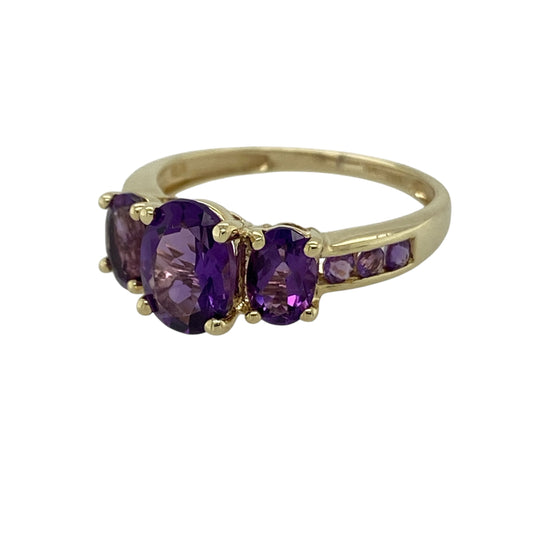 Add rich purple tones and classic elegance to your jewellery collection with this pre-owned 9ct yellow gold amethyst set trilogy ring—an eye-catching piece perfect for everyday wear or special occasions.

Design: The ring features a striking centre amethyst measuring approximately 8mm by 6mm, showcasing beautiful depth of colour and natural brilliance. Amethyst stones are also set along the shoulders, enhancing the trilogy style design and creating a balanced, flowing silhouette across the finger.