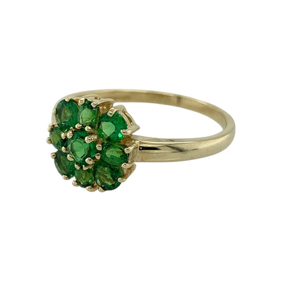 Add vibrant colour and delicate charm to your jewellery collection with this pre-owned 9ct yellow gold green stone flower cluster ring, featuring a classic floral design—perfect for everyday wear or as a thoughtful gift.

Design: The ring showcases a pretty flower cluster arrangement with a green centre stone measuring approximately 3mm, surrounded by additional green stones that form petal-like accents. The floral layout creates a balanced and eye-catching display of rich colour.
