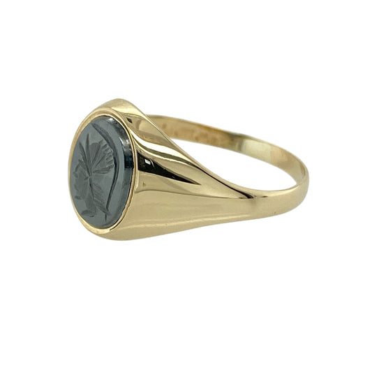 Add bold character and classic style to your jewellery collection with this pre-owned 9ct yellow gold hematite centurion signet ring, featuring a distinctive engraved gemstone—perfect as a statement piece or traditional signet ring.

Design: The ring showcases an oval hematite stone measuring approximately 9mm by 7mm, engraved with a detailed centurion profile. The dark polished surface of the hematite creates a striking contrast against the warm gold band.
