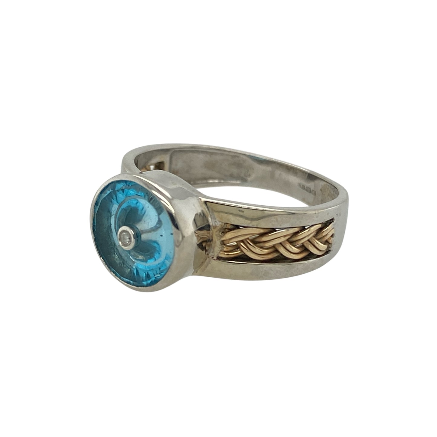 Add bold colour and distinctive detail to your jewellery collection with this pre-owned 9ct white and yellow gold diamond blue stone ring, featuring an eye-catching two-tone design—perfect as a statement dress ring or standout everyday piece.

Design: The ring showcases a striking round blue centre stone measuring approximately 9mm, creating a bold focal point. Diamond accents and plaited detailing across the shoulders add texture and sparkle, enhancing the overall design.
