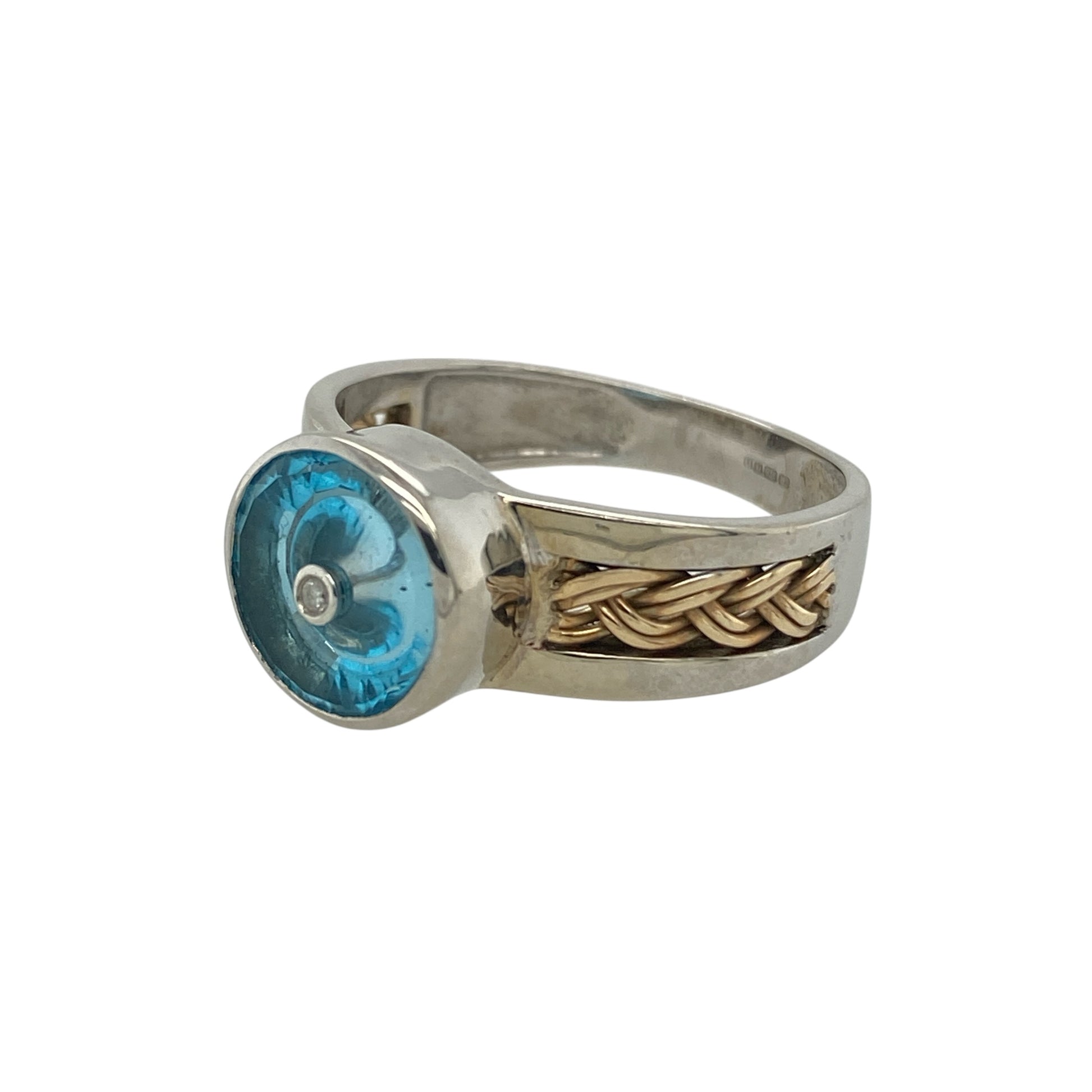 Add bold colour and distinctive detail to your jewellery collection with this pre-owned 9ct white and yellow gold diamond blue stone ring, featuring an eye-catching two-tone design—perfect as a statement dress ring or standout everyday piece.

Design: The ring showcases a striking round blue centre stone measuring approximately 9mm, creating a bold focal point. Diamond accents and plaited detailing across the shoulders add texture and sparkle, enhancing the overall design.
