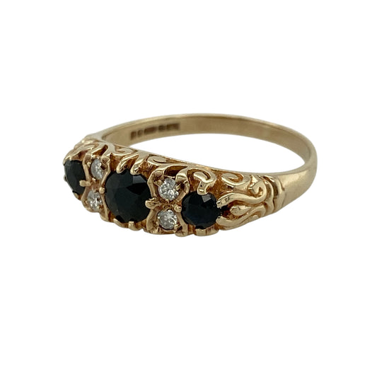 Add timeless elegance and rich colour to your jewellery collection with this pre-owned 9ct yellow gold diamond and sapphire trilogy ring, featuring classic gemstones and refined sparkle—perfect for special occasions or everyday wear.

Design: The ring showcases three round sapphires, with the centre stone measuring approximately 4mm in diameter and the two side stones approximately 3mm each, complemented by two diamonds set between each sapphire for added brilliance.