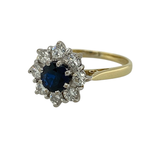 Add timeless elegance and floral-inspired charm to your jewellery collection with this pre-owned 18ct yellow gold diamond and sapphire cluster ring, featuring a classic design with rich colour and sparkle—perfect for special occasions or refined everyday wear.

Design: The ring features a round sapphire measuring approximately 5mm in diameter at its centre, surrounded by sparkling diamonds arranged in a flower-style cluster for a soft and eye-catching look.
