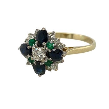 Add vibrant colour and luxurious sparkle to your jewellery collection with this pre-owned 18ct yellow gold diamond, sapphire and emerald cluster ring, featuring a bold and eye-catching design—perfect for special occasions or statement wear.

Design: The ring features a central diamond surrounded by a mix of sapphires, emeralds, and additional diamonds, creating a rich and colourful cluster with striking contrast and brilliance.