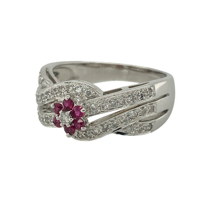 Add luxurious sparkle and rich colour to your collection with this pre-owned 14ct white gold diamond and ruby set flower cluster band ring—an eye-catching piece with elegant detail and timeless appeal.

Design: The ring features a 9mm wide front with a delicate flower cluster at the centre, formed by a small ruby surrounded by sparkling diamonds. The shoulders are designed with crossover open bands, set with additional diamonds for enhanced brilliance and a layered look.