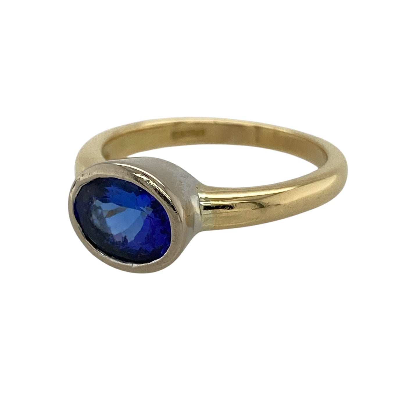 Bring bold colour and refined elegance to your collection with this pre-owned 18ct yellow gold blue stone solitaire ring, featuring a striking centrepiece with contemporary detailing—perfect for special occasions or standout everyday wear.

Design: The ring showcases a 9mm by 7mm oval blue stone at the centre, presented in a white gold rubover style for a smooth, modern finish and a clean, defined look.