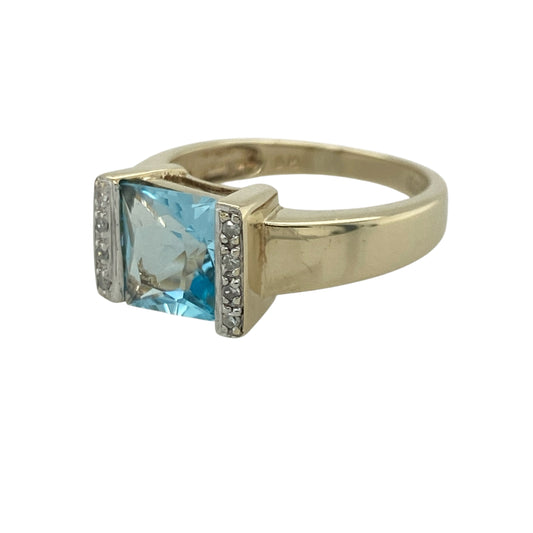 Add vibrant colour and exceptional sparkle to your jewellery collection with this pre-owned 9ct yellow gold diamond and blue topaz ring, featuring a striking gemstone design with elegant statement appeal—perfect for special occasions, gifting, or sophisticated everyday wear.

Design: The ring showcases a stunning square-cut blue topaz measuring approximately 8mm by 8mm, creating a bold and eye-catching focal point.