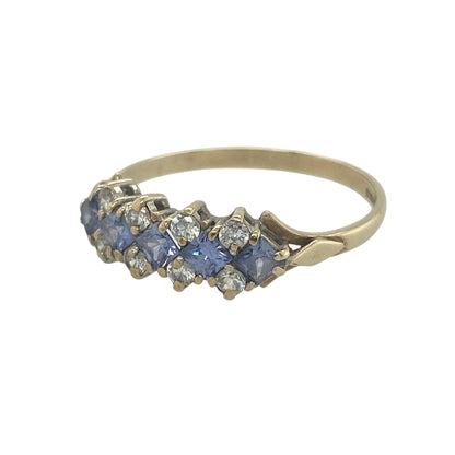 Elegant and colourful, this pre-owned 9ct yellow gold tanzanite and cubic zirconia cluster band ring offers a beautiful combination of vibrant gemstones and sparkling accents. Its contemporary design and eye-catching colour contrast make it a stylish addition to any jewellery collection.

Design: The ring features a wide cluster-style band with a striking arrangement of square-cut tanzanite stones running through the centre.