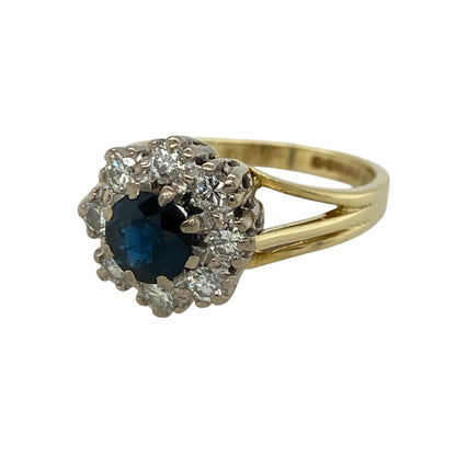 This pre-owned 18ct yellow gold diamond and sapphire cluster ring is a timeless design, showcasing a vibrant sapphire surrounded by sparkling diamonds.

Design: The ring features a round centre sapphire framed by a dazzling halo of diamonds, creating a classic cluster design that offers exceptional brilliance. Its elegant appearance makes it a perfect choice for both everyday wear and special occasions.
Material: Made from 18-carat yellow gold.