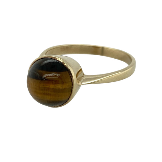 This pre-owned 9ct yellow gold tiger's eye ring showcases a striking round tiger's eye gemstone with its distinctive natural chatoyancy.

Design: The ring features a large round tiger's eye gemstone, displaying the warm golden brown tones and silky band of light that make this gemstone so recognisable. Its classic setting allows the gemstone to take centre stage, creating a bold yet timeless look.
Material: Made from 9-carat yellow gold.